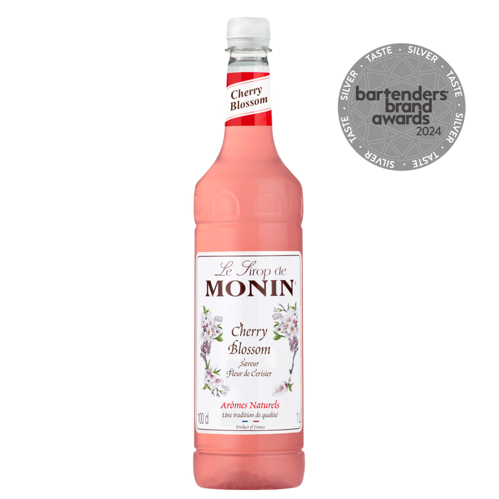 A bottle of MONIN Cherry Blossom syrup, featuring a white label with cherry blossom illustrations and text, captures the essence of Japanese culture. Adorning the display is a medallion marked "bartenders brand awards 2024," encircled by the word "SILVER." This syrup has a light pink hue that evokes the spirit of O-Hanami celebrations.