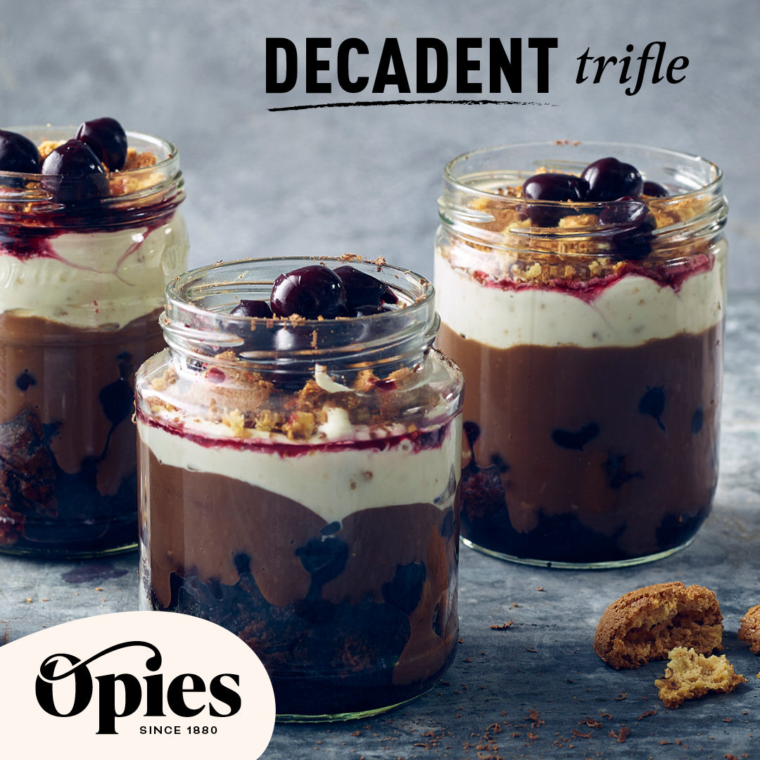 Three glass jars filled with a layered decadent trifle featuring luxurious Opies Black Cherries with Kirsch, chocolate, and cream. Each jar is topped with cherries and a crumbled biscuit. The text "DECADENT trifle" is at the top, and the Opies logo is at the bottom left. The background is gray.