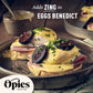 A close-up of Eggs Benedict topped with circular slices of black pudding and garnished with chives. The dish is served on a rustic plate, with a bowl of Opies Pickled Walnuts in the background. Text reads, "Adds ZING to EGGS BENEDICT." Opies logo and “Since 1880” are displayed.